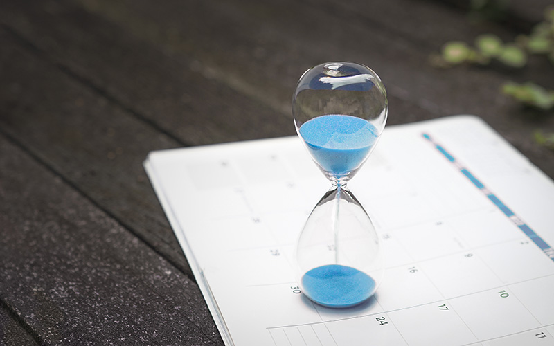 Hourglass and calendar on dark wood background.