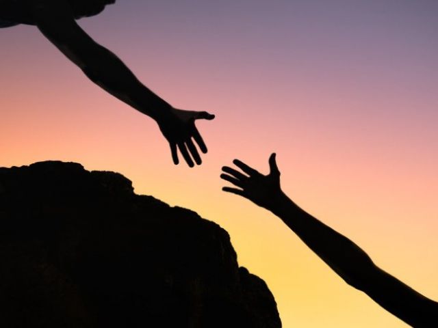 silhouette of two hands reaching for each other offering help in the climb