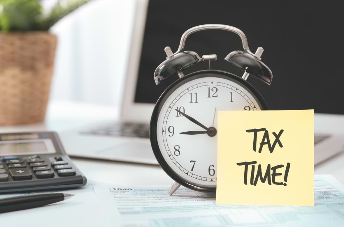 An alarm clock with a posted note that has tax time written on it An alarm clock with a posted note that has tax time written on it